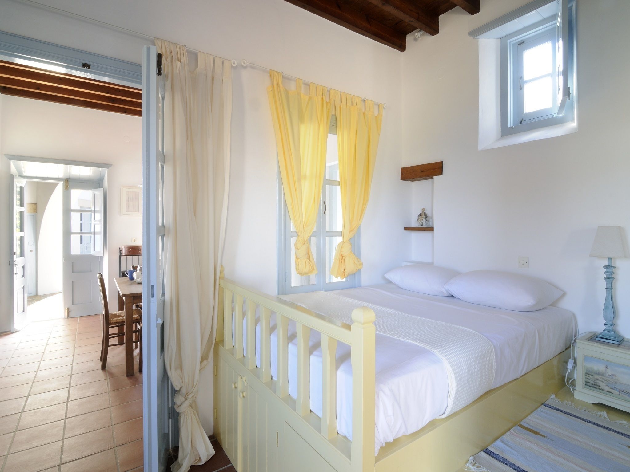 A bedroom with a bed, a window with curtains, a bedside table with a lamp, and a chair.