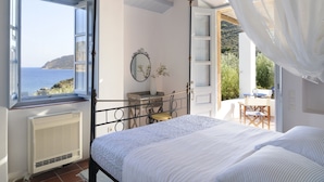 A bedroom with a four-poster bed, a view of the sea, and a balcony with outdoor furniture. - Onar (Patmos)