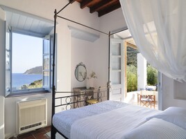 Un dormitorio con cama con dosel, vistas al mar y un balcón con mobiliario exterior.