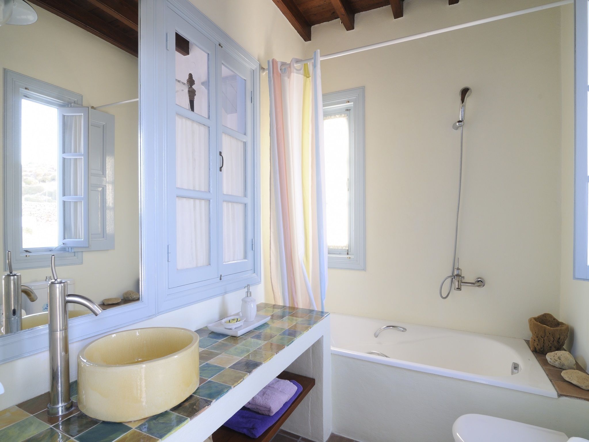 A bathroom with a bathtub, a sink with a large basin, a shower, and a window with curtains.