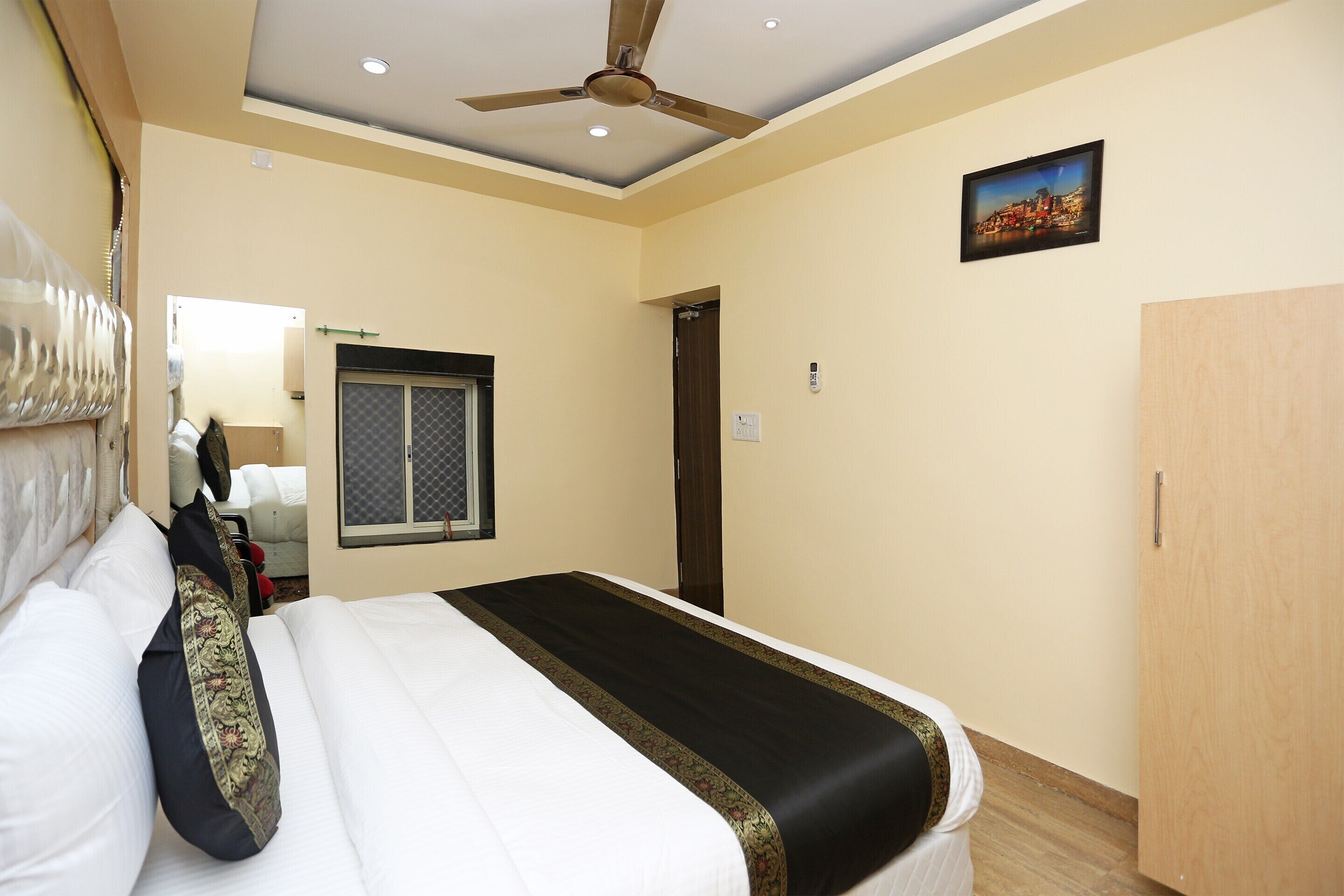 A hotel room with a bed, a ceiling fan, a window with a view, and a door.