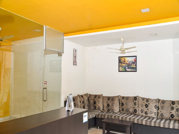 Habitación de hotel con mostrador de recepción, sofá, ventilador de techo y un cuadro colgado en la pared.