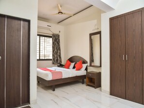 A bedroom with a bed, a nightstand, a wardrobe, a ceiling fan, and a window with curtains. - OYO 12854 Hotel Sahara Inn (Nashik)