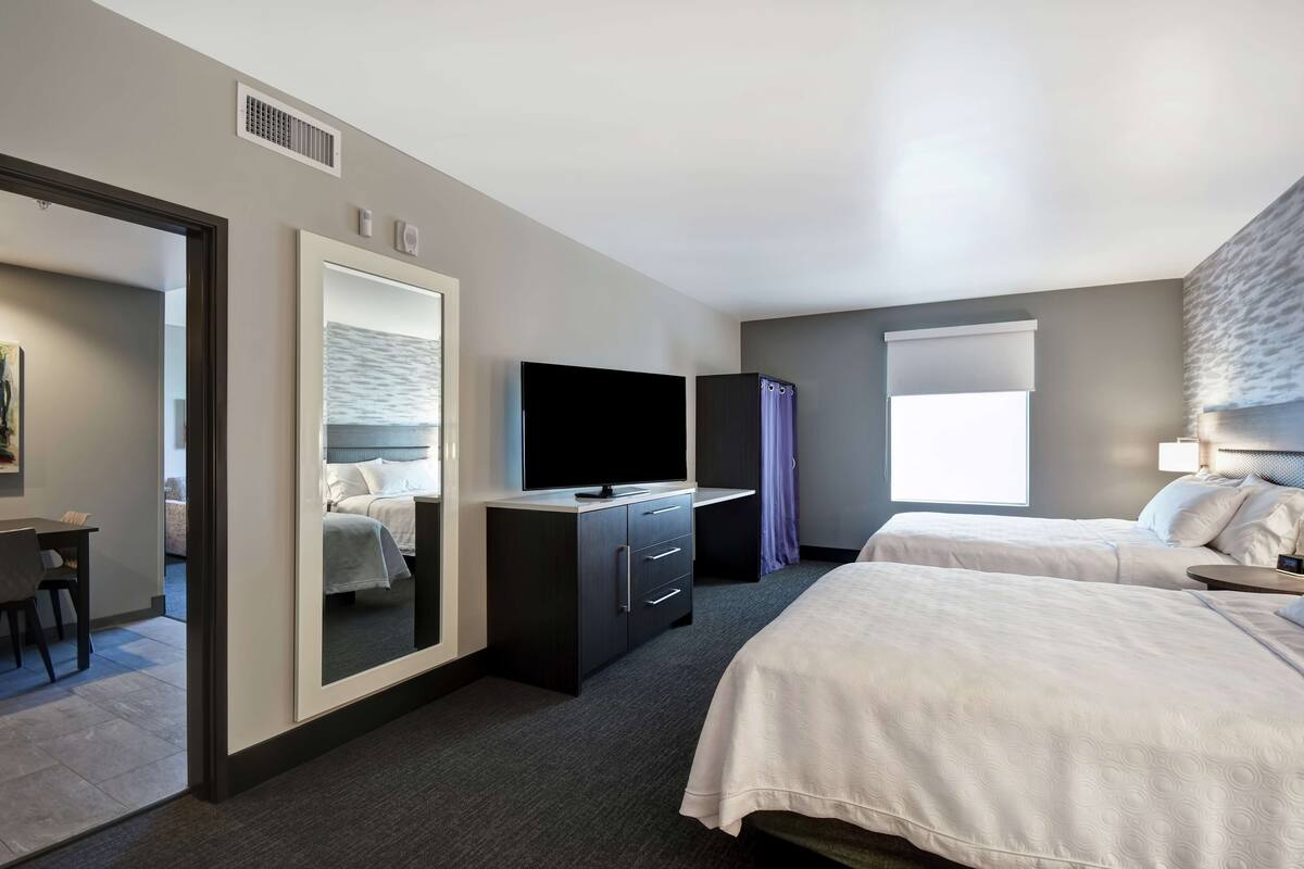 Ein Hotelzimmer mit zwei Betten, einem Fernseher, einem Schreibtisch und einem großen Spiegel.