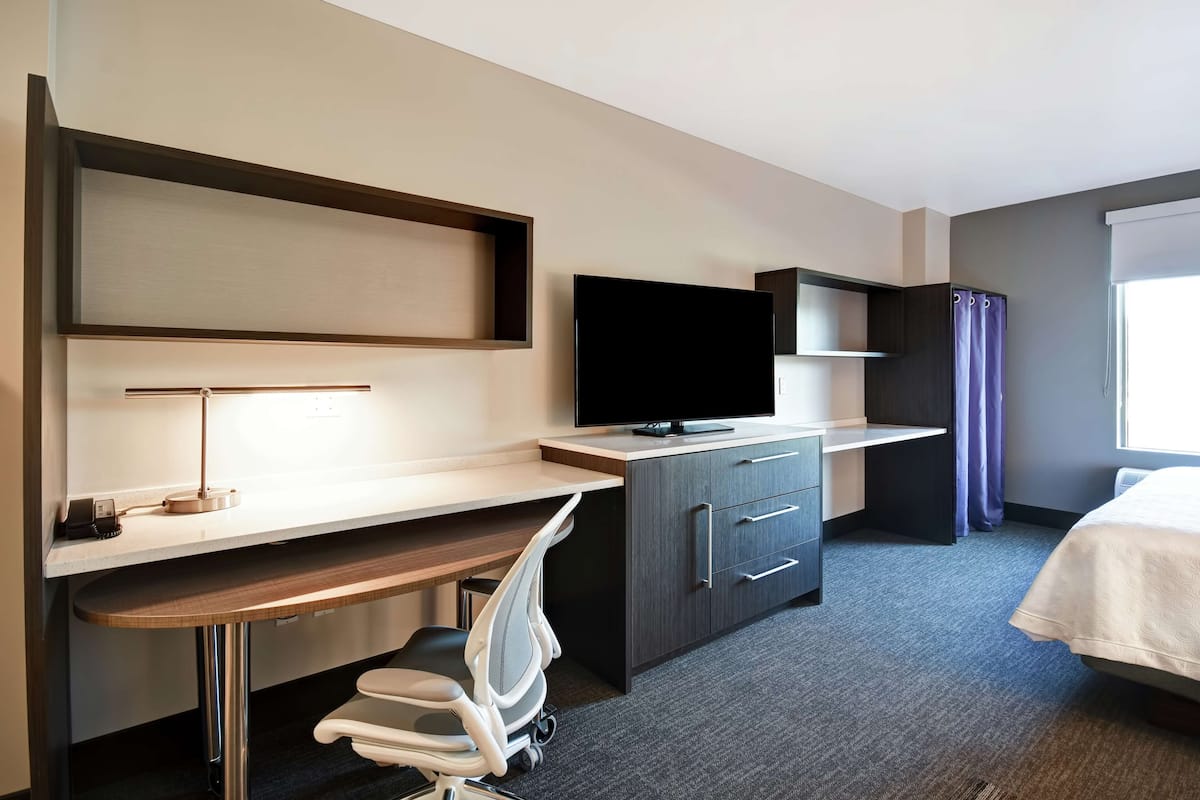Ein Hotelzimmer mit Schreibtisch, Stuhl, Fernseher, Kleiderschrank und einem Bett.