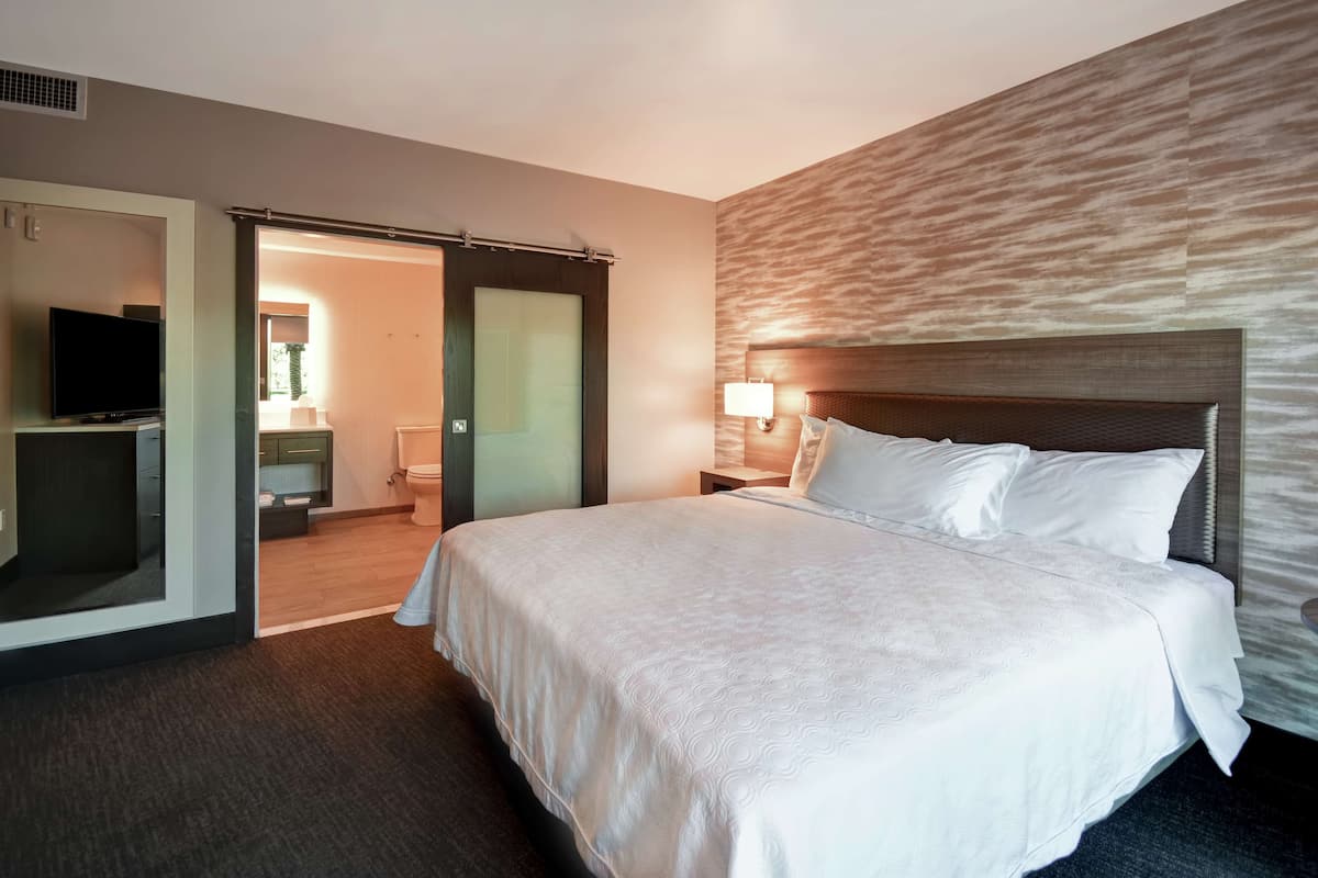 Ein Hotelzimmer mit einem großen Bett, einem Fernseher, einem Badezimmer und einer Schiebetür zu einem Balkon.