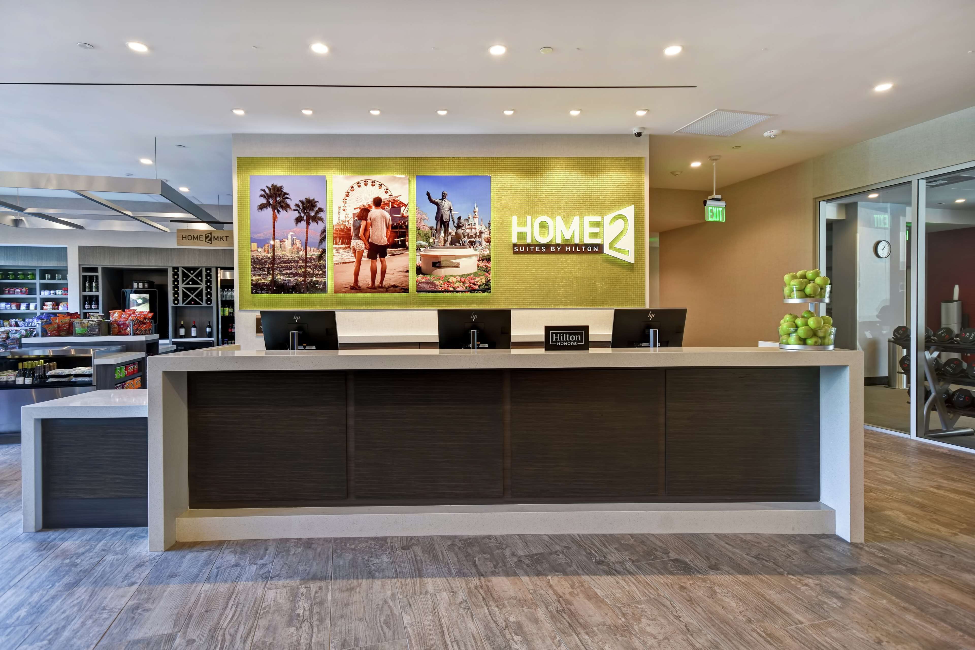 Een hotel receptiebalie met een groot bord waarop 'HOME2 Suites by Hilton' staat.