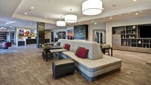 A modern hotel lobby with a sectional sofa, dining area, and a TV wall. - Home2 Suites by Hilton Los Angeles Montebello (Montebello)