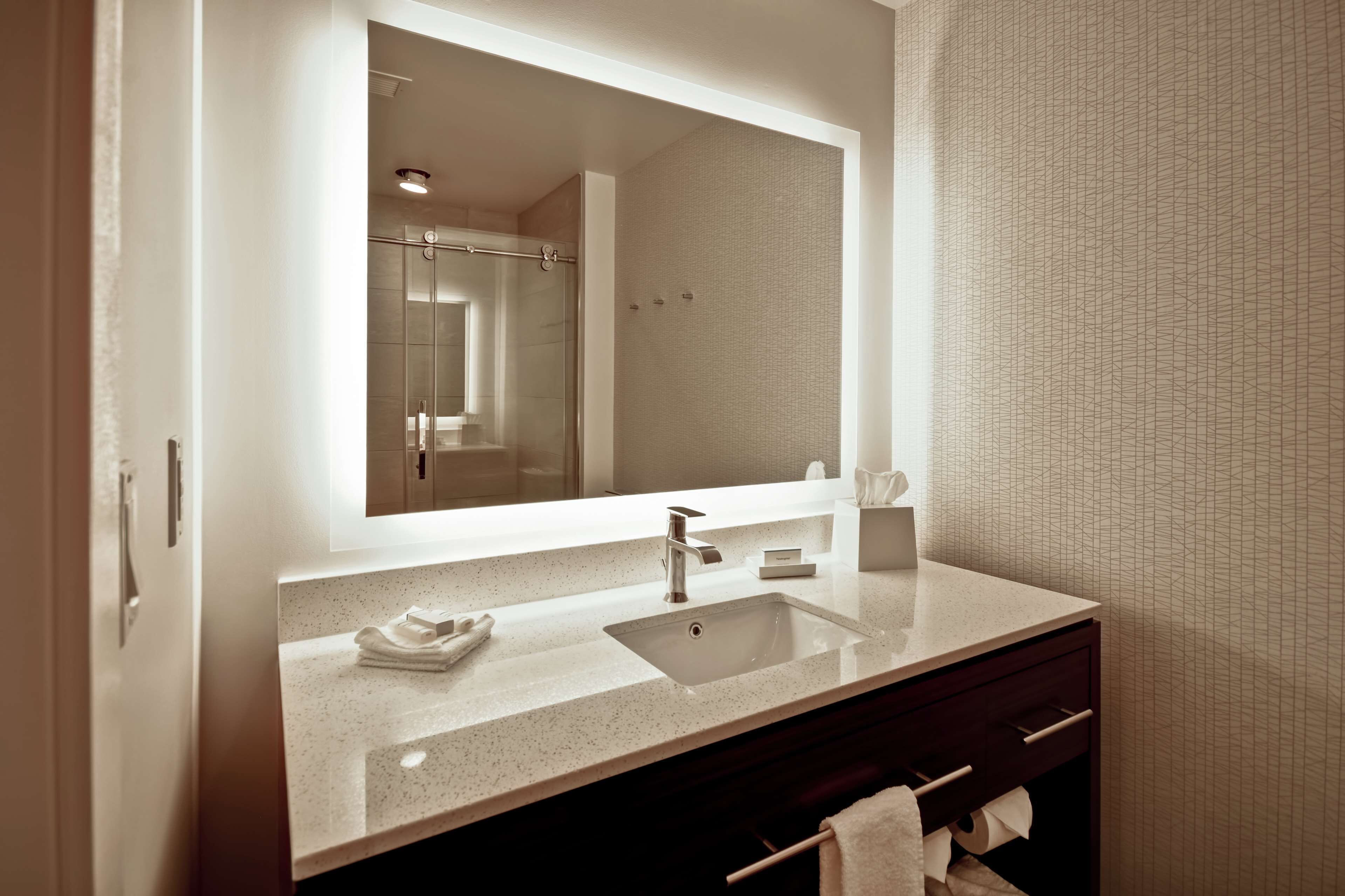 A modern bathroom with a large mirror, a sink, and a shower.