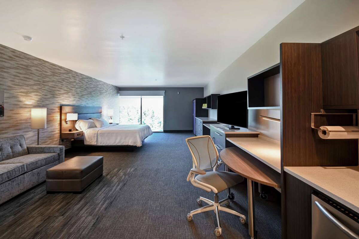 Ein modernes Hotelzimmer mit einem Bett, einem Schreibtisch mit Stuhl, einer Couch und einem Fernseher.