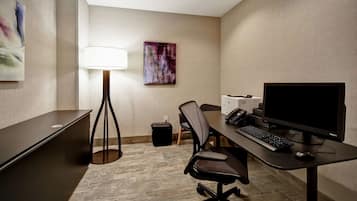 A hotel room with a desk, computer, chair, lamp, and artwork on the wall.