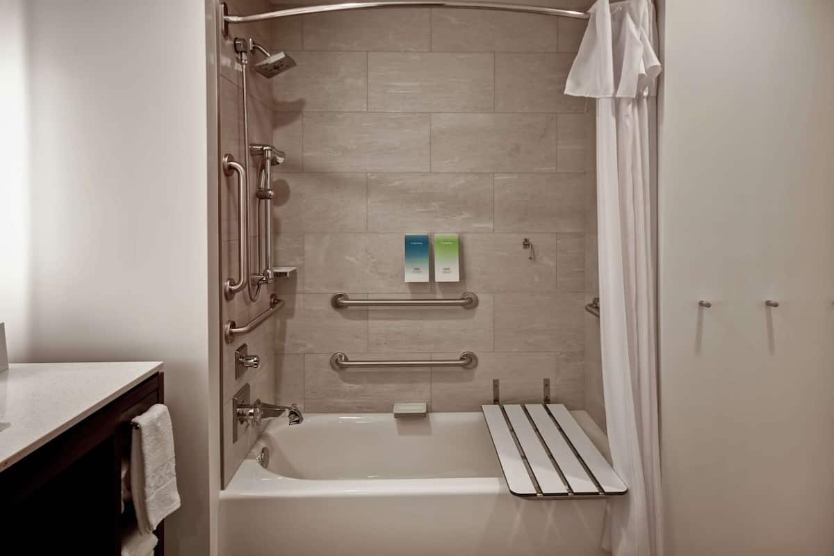 A modern bathroom with a bathtub, grab bars, and a showerhead.