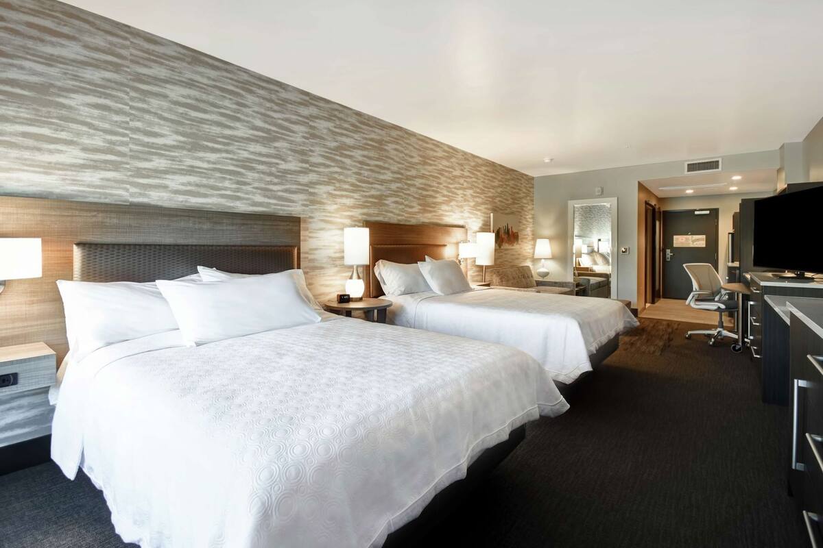 A hotel room with two beds, a desk, a chair, and a television.