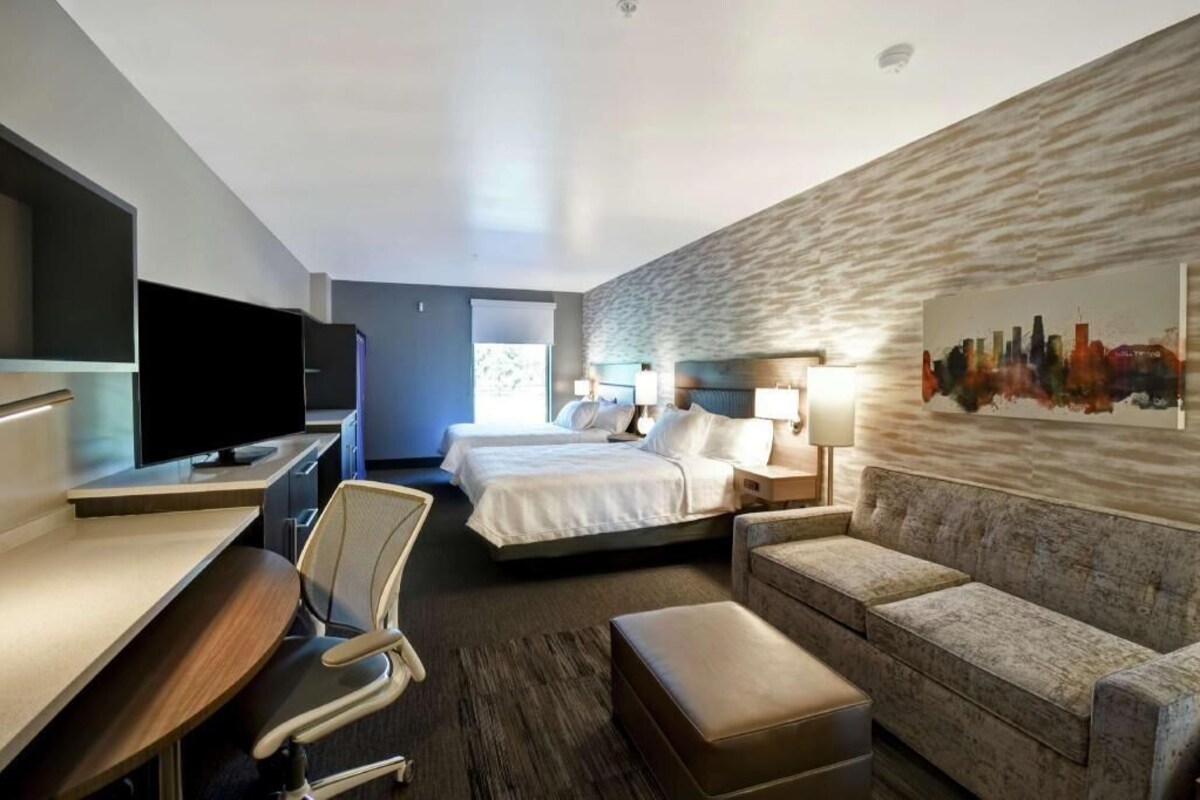 Une chambre d’hôtel avec un lit, un bureau avec une télévision, un canapé et un tableau représentant un paysage urbain accroché au mur.