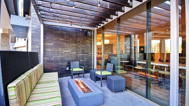 A modern outdoor seating area with a fire feature, wicker furniture, and a view into the building. - Home2 Suites by Hilton Los Angeles Montebello (Montebello)