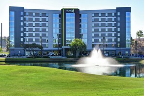 Een modern hotel met een fontein in het midden, een verzorgd gazon en een parkeerplaats.