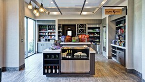 A modern retail space with a central island displaying wine bottles and snacks, surrounded by shelves stocked with various products. - Home2 Suites by Hilton Los Angeles Montebello (Montebello)