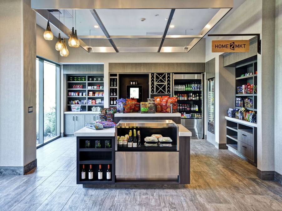 A modern retail space with a central island displaying wine bottles and snacks, surrounded by shelves stocked with various products.