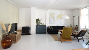 A modern living room with a television, a black sofa, a green armchair, a world map on the wall, and a large mirror. - Solferie Holiday Apt. Henrik Wergelands (Kristiansand)