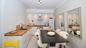 A modern kitchen with a dining area, featuring a black dining table, white chairs, and a yellow chair. - Solferie Holiday Apt. Henrik Wergelands (Kristiansand)