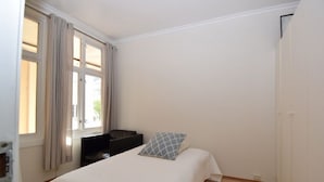 A bedroom with a bed, a window with curtains, a wardrobe, and a small seating area. - Solferie Holiday Apt. Henrik Wergelands (Kristiansand)