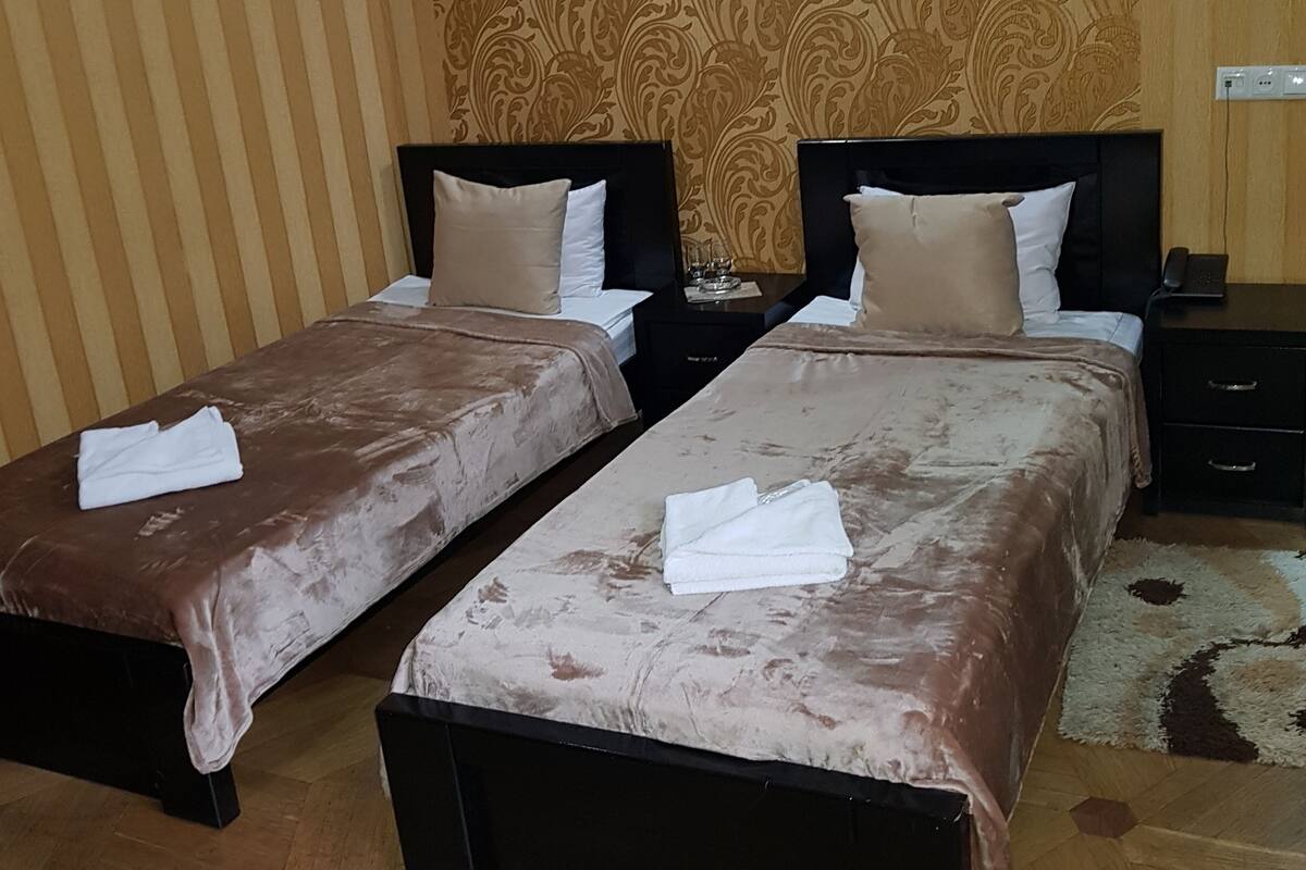 A hotel room with two beds, a nightstand, a lamp, and a patterned wallpaper.