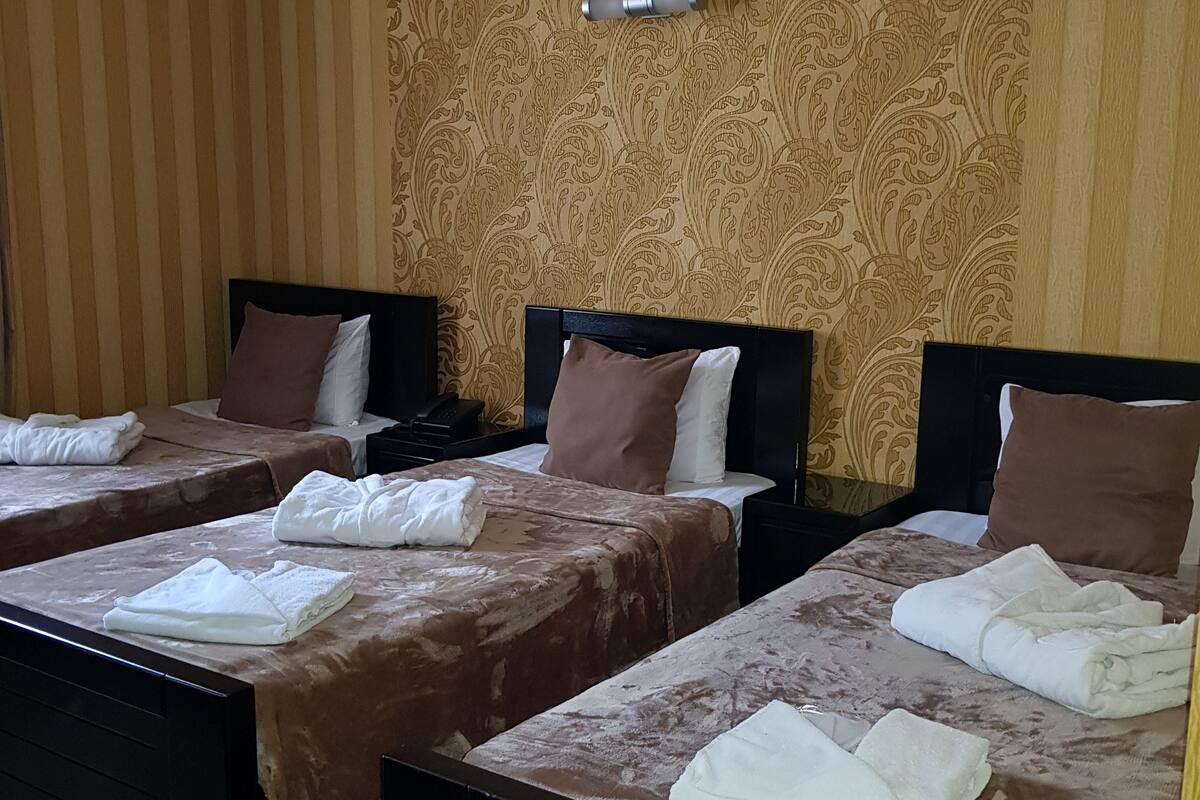 A hotel room with three beds, each with a brown bedspread and white towels. The room has wooden paneling on the walls and a patterned wallpaper.