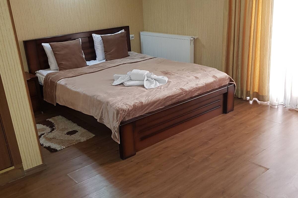 A bedroom with a wooden bed, beige walls, a radiator, and a window with curtains.