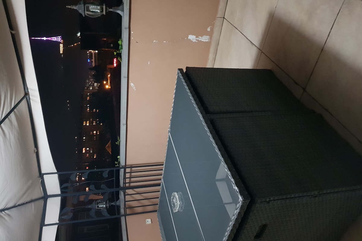 A balcony with a view of a cityscape at night, including a tower with lights.