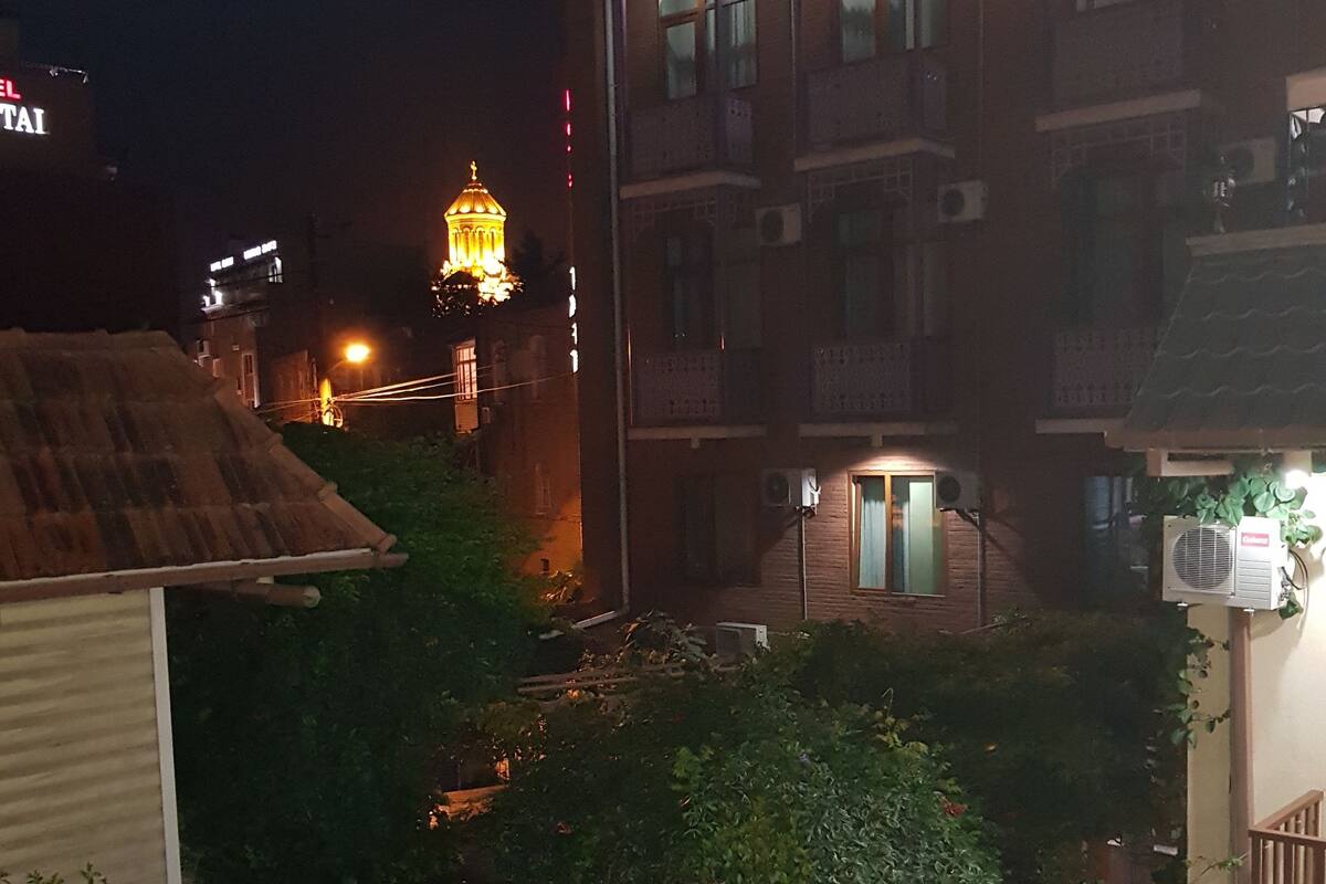 A night view of a building with multiple windows and balconies, surrounded by greenery.