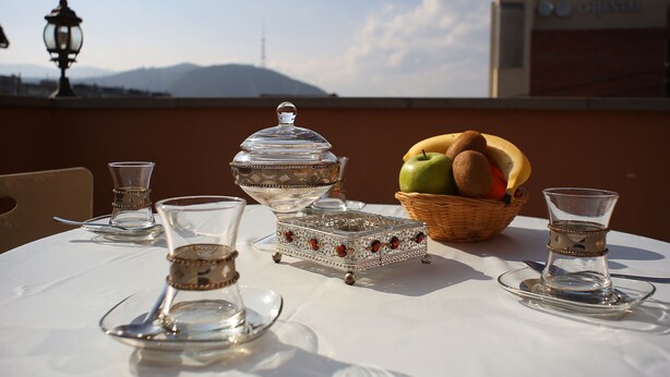 A table set with a clear glass pitcher, a glass carafe, a silver tray with red accents, a fruit basket, and a glass of water. - Hotel Danisimo (Tbilisi)