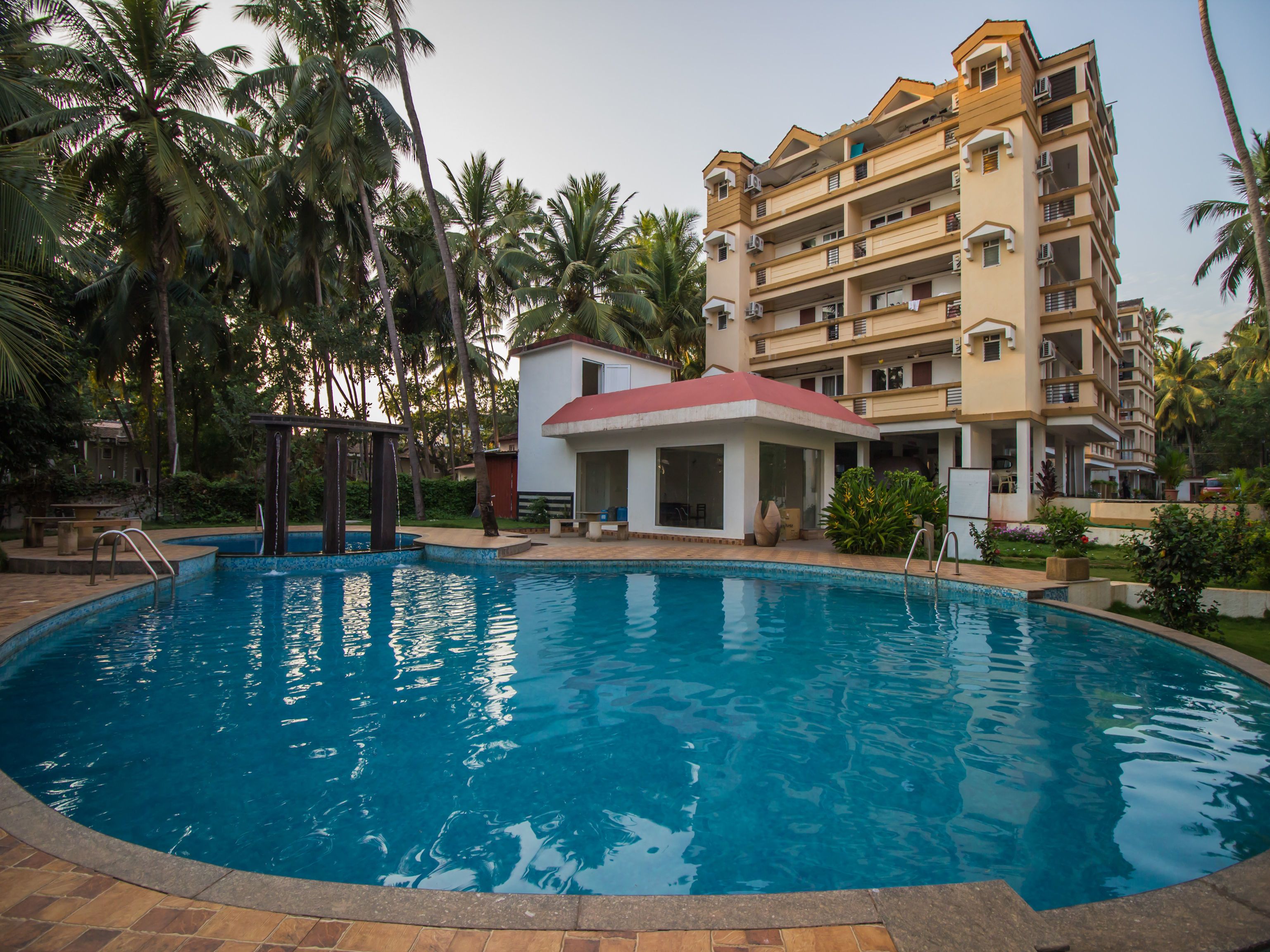 A swimming pool surrounded by palm trees and a multi-story building with balconies.
