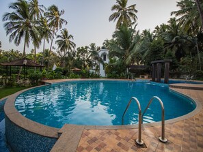 A swimming pool with a tiled edge, surrounded by palm trees and a gazebo. - OYO 12953 Home Pool View 2BHK Arpora (Arpora)