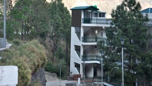 Un immeuble à plusieurs étages doté de balcons, entouré d’arbres et situé dans un paysage vallonné.