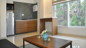 Une cuisine moderne équipée d’un réfrigérateur, de meubles en bois et d’un four encastré. Une fenêtre offre une vue sur les arbres, et une petite table est agrémentée d’un vase de fleurs.