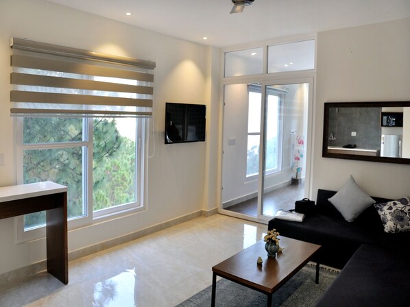 Una sala de estar moderna con un ventanal grande, un televisor de pantalla plana, un sofá de color oscuro y una mesa de centro con un jarrón.