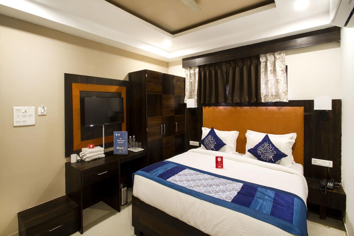 Een hotelkamer met een bed, een bureau, een kledingkast, een televisie en een plafondventilator.
