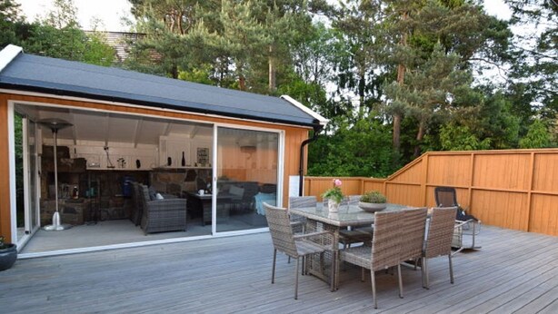 Een terras met een glazen patio, rieten meubilair en een houten omheining.