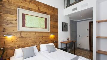 A hotel room with a wooden headboard, a large framed map, a bed with white linens, a desk with a chair, and a small plant.