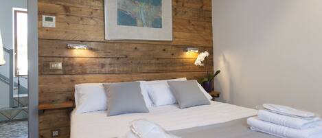 A neatly made bed with grey and white linens, a wooden headboard, and a framed artwork above.