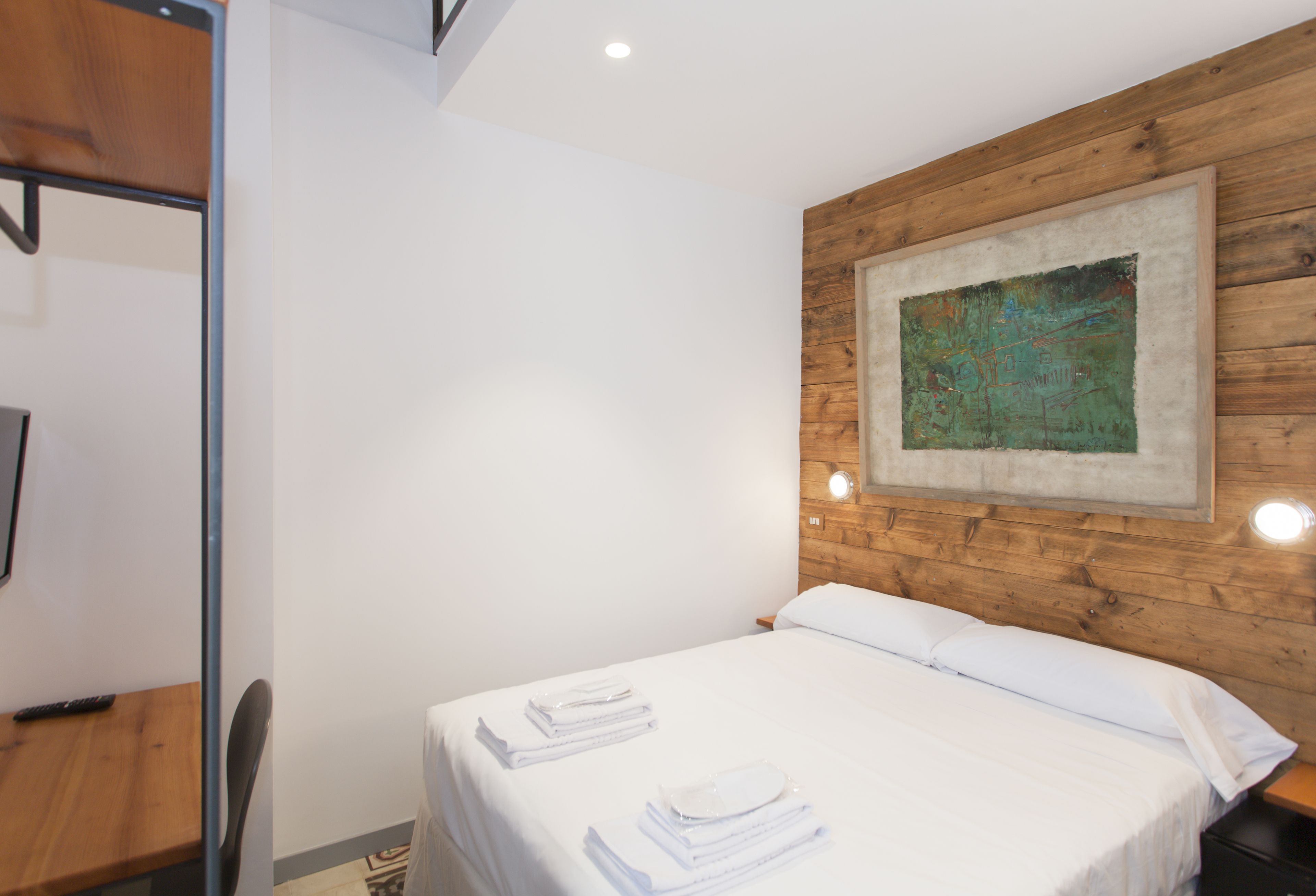 A neatly made bed with white linens and towels, a wooden headboard, and a painting on the wall.