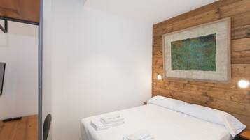 A neatly made bed with white linens and towels, a wooden headboard, and a painting on the wall.