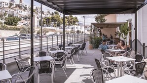 An outdoor cafe with tables and chairs, overlooking a street with cars and buildings.