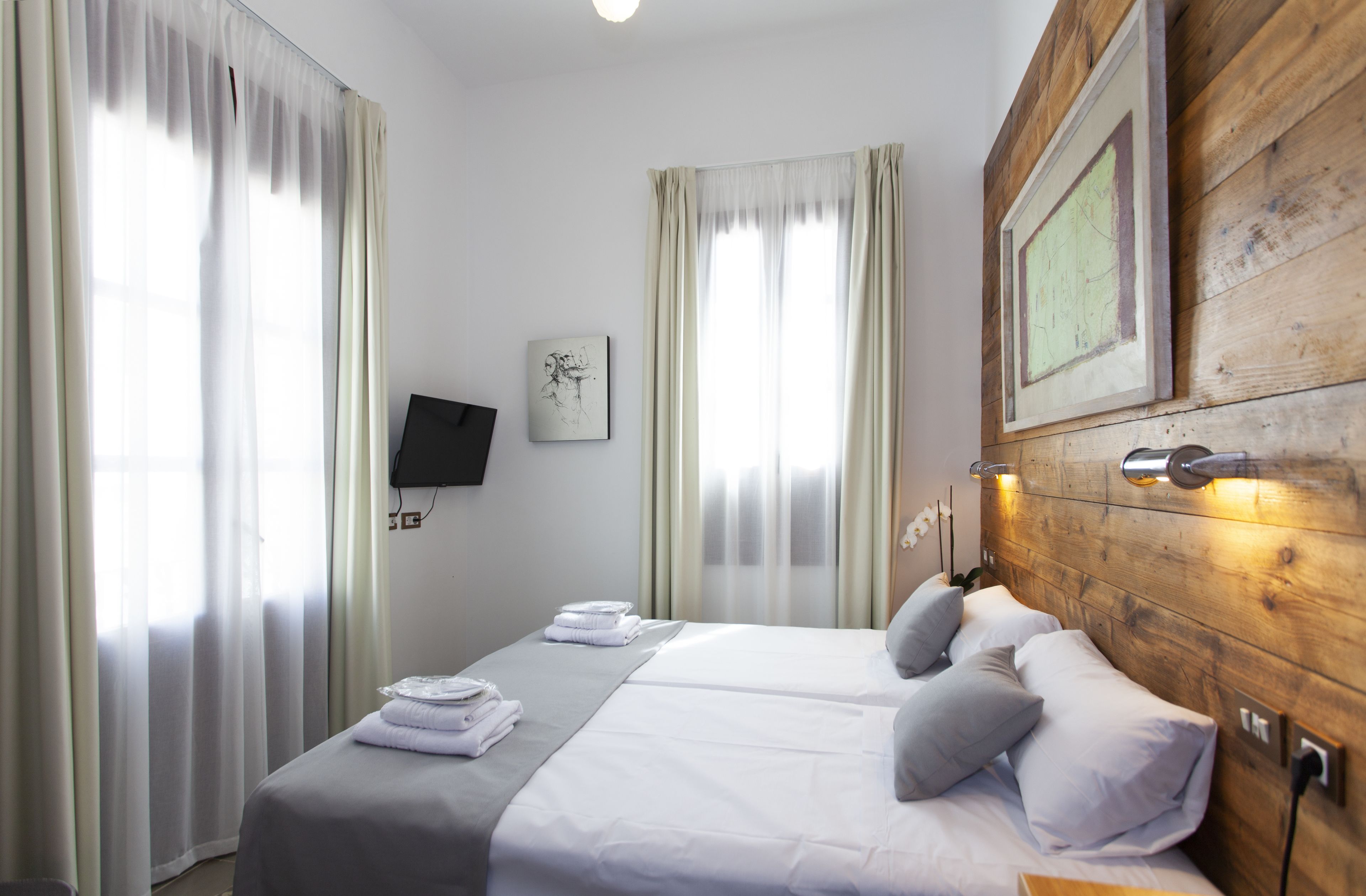 Ett hotellrum med en sänggavel i trä, en säng med vita sängkläder, två kuddar, en platt-TV som är monterad på väggen och en inramad karta.