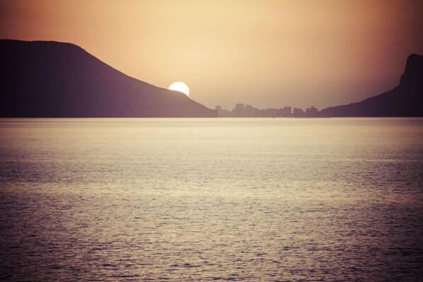 Una masa de agua tranquila con un atardecer y siluetas de colinas al fondo.