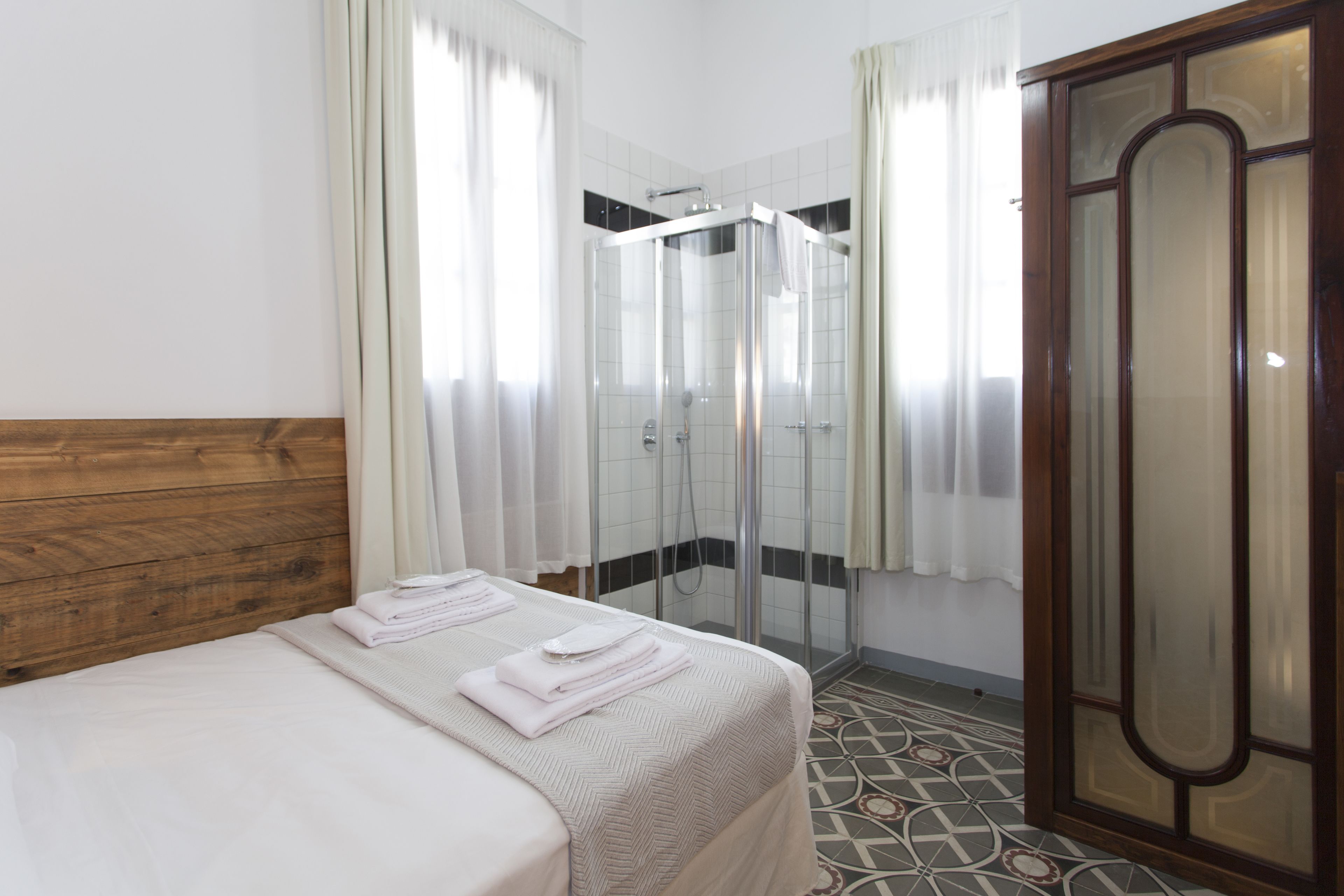 A hotel room with a bed, a shower, and a wardrobe.