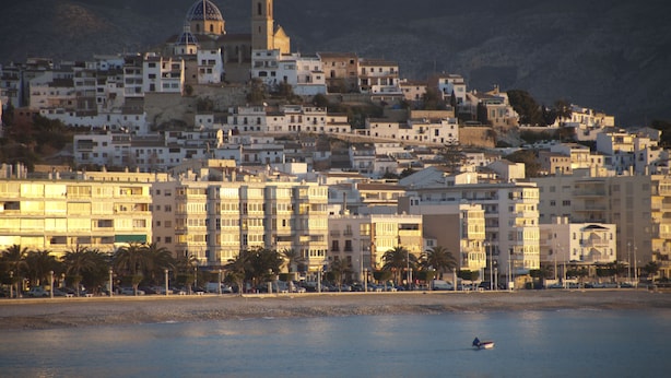 A coastal cityscape with a prominent hilltop church and a small boat on the water.