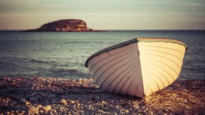A boat on a pebbled beach with calm water and a distant island.