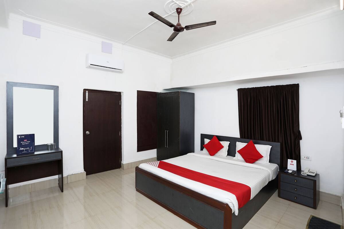 Quarto com cama, mesa de cabeceira, guarda-roupa e ventoinha no teto.