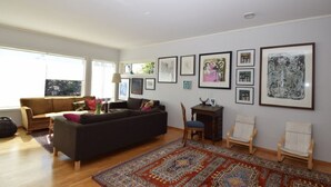 Uma sala de estar espaçosa com um sofá escuro, uma mesa de centro de madeira e um tapete estampado.